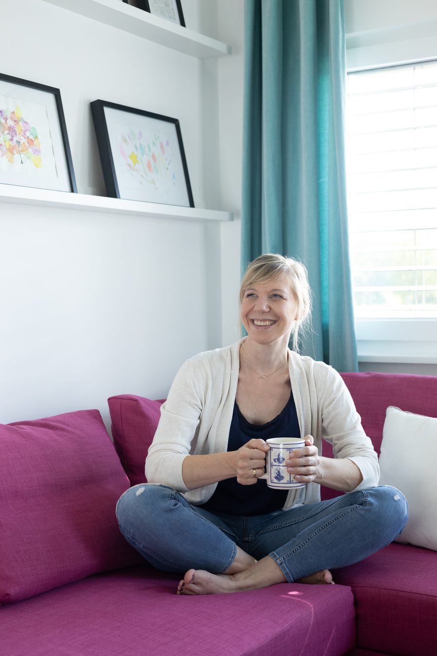 Janneke Duijnmaijer sitzt lächelnd mit einer Tasse auf ihrem Sofa